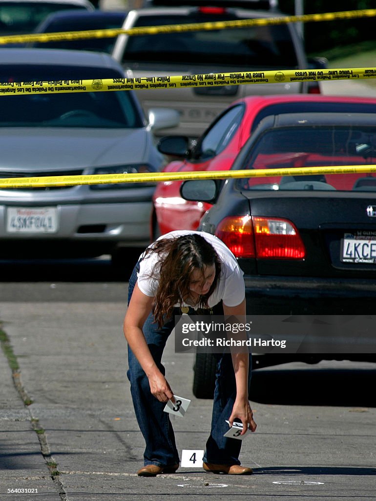 A female law enforcement officer picks up bullet shell markers at the scene where LAPD and LA City
