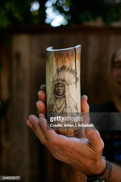 Schrimshander Ray Caruso holds a fossil ivory wooly mammoth tusk with Native American face at his Laguna Beach studio. He's an exhibiter at the...