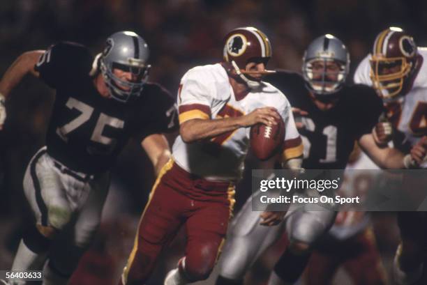 Joe Theismann of the Washington Redskins scrambles to avoid two rushing Oakland Raiders' Howie Long and teammate during Super Bowl XVIII against the...