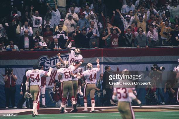 Jerry Rice, wide receiver of the San Francisco 49ers, jumps and celebrates in the end zone with teammates Matt Millen, Jesse Sapolu, and Tom Rathman...