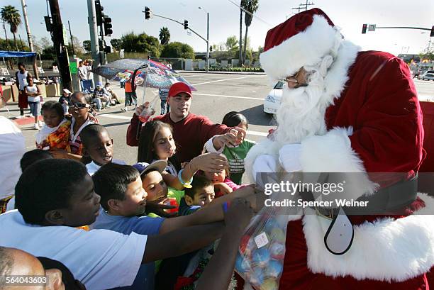 Greg Brown,right, as Santa, hands out small toys to children gathered along Central Avenue in Watts, Saturday, December 2 for the 41st Annual...