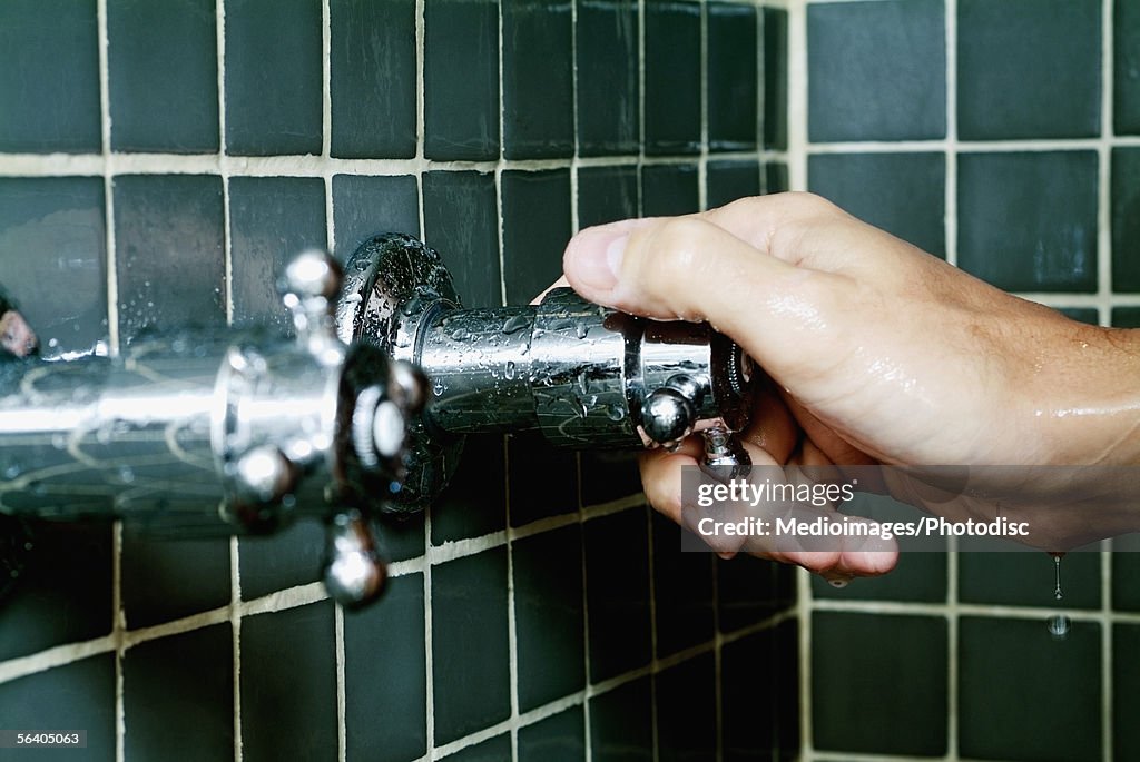 Close-up of a person's hand turning a shower knob