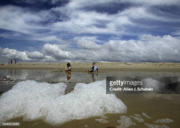 Mimicking the shape of clouds, sea foam washes ashore as vacationers Skylar Cannon, left, and brother Zach Cannon of Seattle, WA, enjoy a break from...