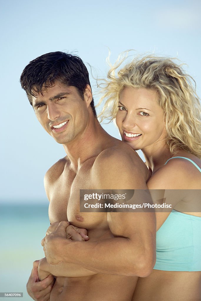 Side profile of a young woman embracing a young man from behind on the beach