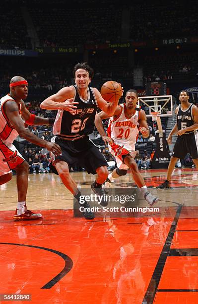 Manu Ginobili of the San Antonio Spurs drives past Al Harrington of the Atlanta Hawks during a game on December 10, 2005 at Philips Arena in Atlanta,...