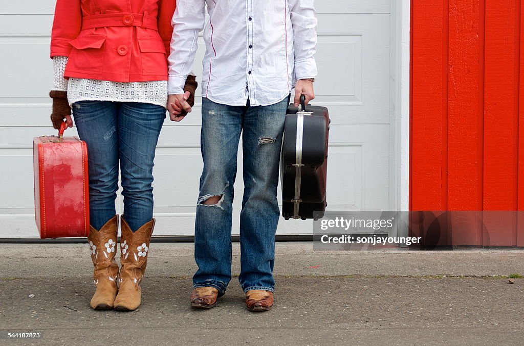 Low section of couple holding a suitcase and guitar case