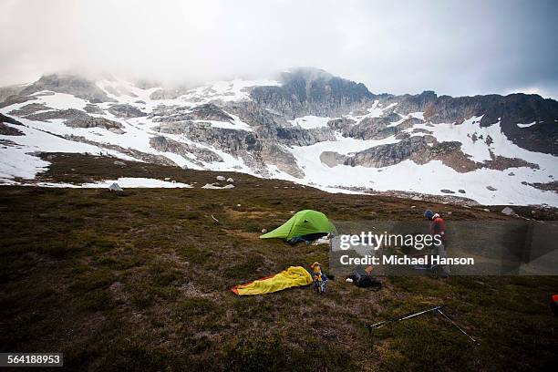 a climber sets up a campsite beneath low hanging clouds. - wildnisgebiet glacier peak stock-fotos und bilder
