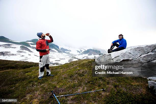 two climbers enjoy a bottle of bourbon while resting before attempting to climb a peak. - wildnisgebiet glacier peak stock-fotos und bilder