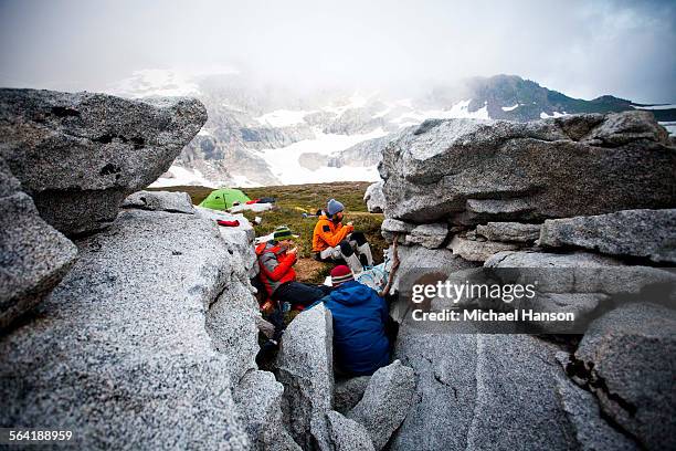 three climbers eat dehydrated food between rocks hoping to avoid the wet conditions - wildnisgebiet glacier peak stock-fotos und bilder