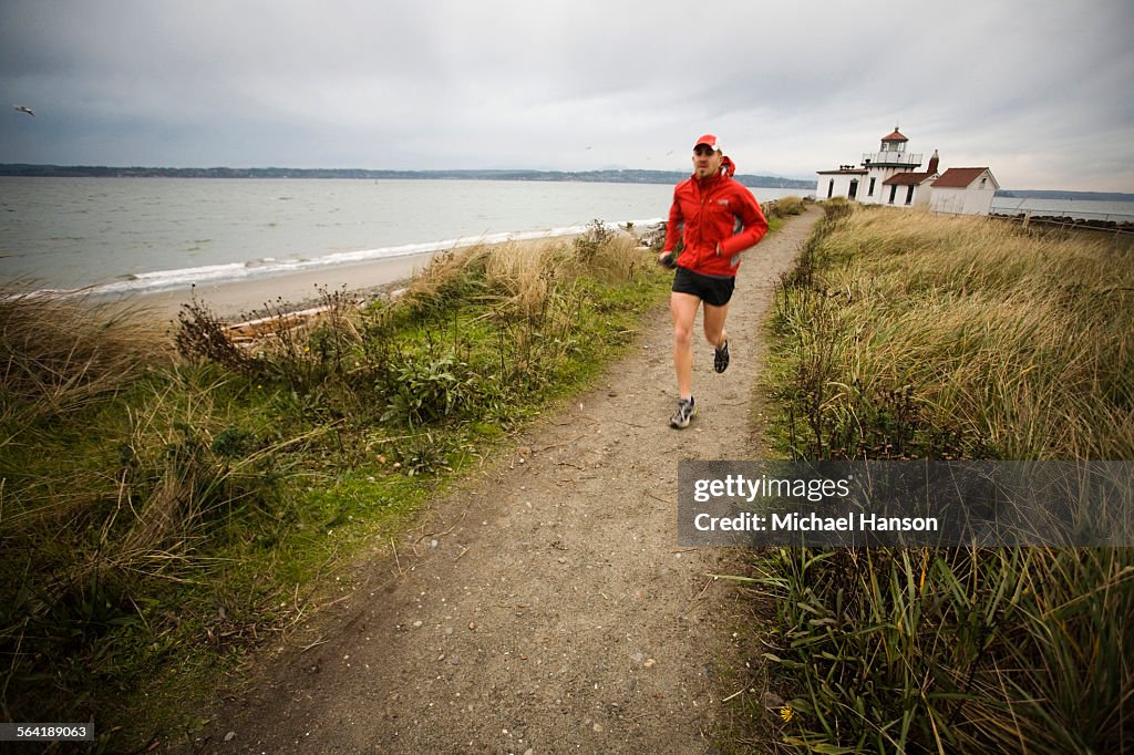 A runner follows a trail along the Puget Sound at Discovery Park, Seattle, WA.