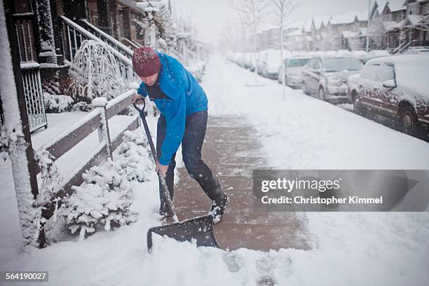 a man shovels the sidewalk outside of his suburban house. - schop stockfoto's en -beelden