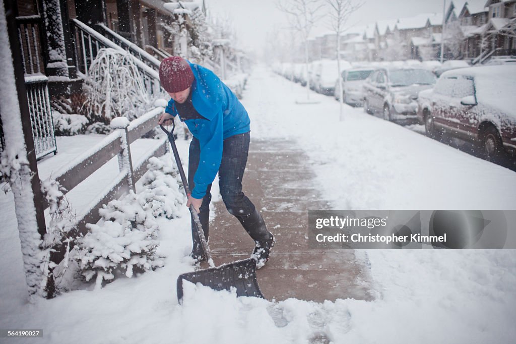 A man shovels the sidewalk outside of his suburban house.