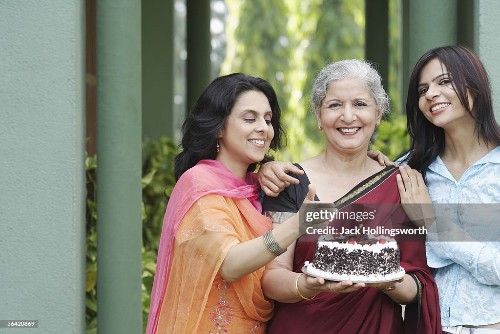 Portrait of a mature woman holding a cake with a young woman and a mid adult woman standing beside her