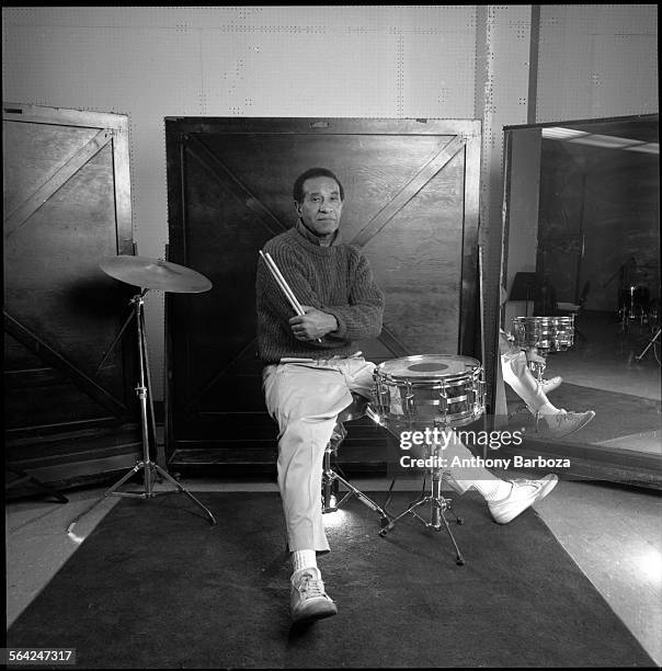 Portrait of American jazz musician Max Roach , dressed in a sweater, as he poses behind a drum kit with his drumsticks in his hand, 1989.