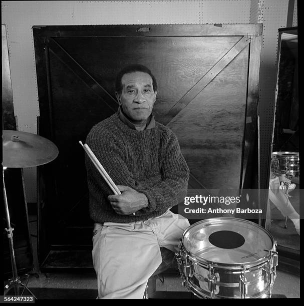 Portrait of American jazz musician Max Roach , dressed in a sweater, as he poses behind a drum kit with his drumsticks in his hand, 1989.