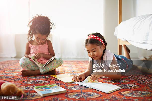 Two sisters reading books on the floor in bedroom