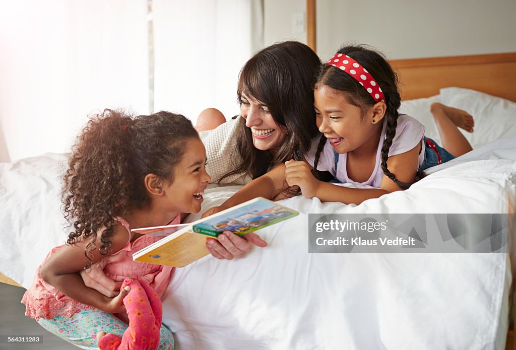 Mother & 2 kids lauging & reading in bedroom