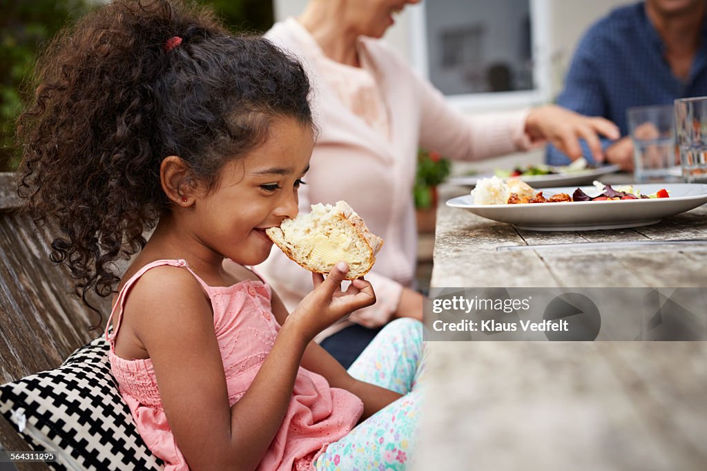 Cute girl taking bite of bread at outside dinner