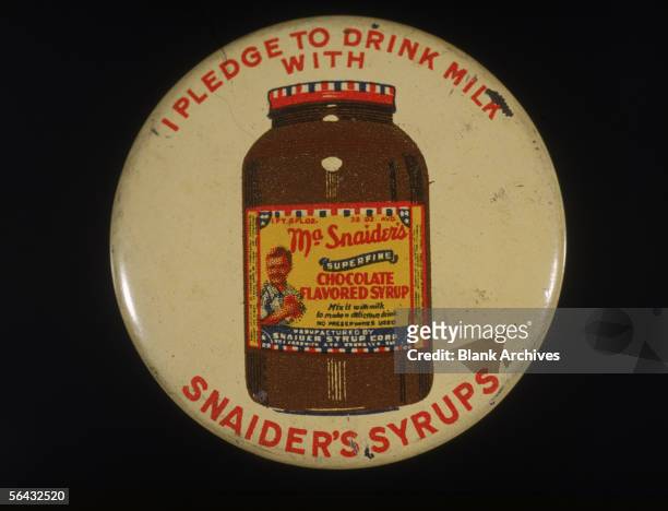 View of a button advertising Snaider's Syrups, 1960s. It reads 'I Pledge to Drink Milk with Snaider's Syrups' and includes an illustration of a...