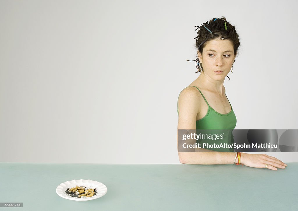 Young woman looking over shoulder at ashtray full of cigarette butts