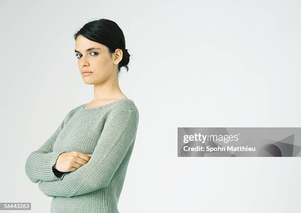 young woman standing with arms crossed, looking at camera - suspicion fotografías e imágenes de stock