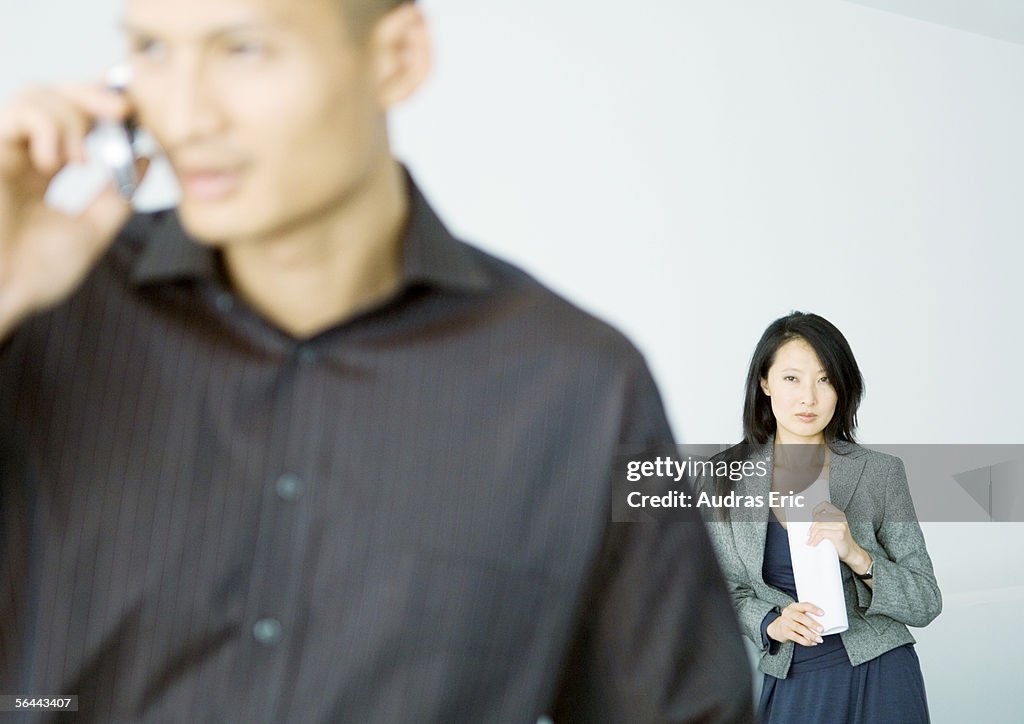 Businesswoman standing behind man talking on cell phone