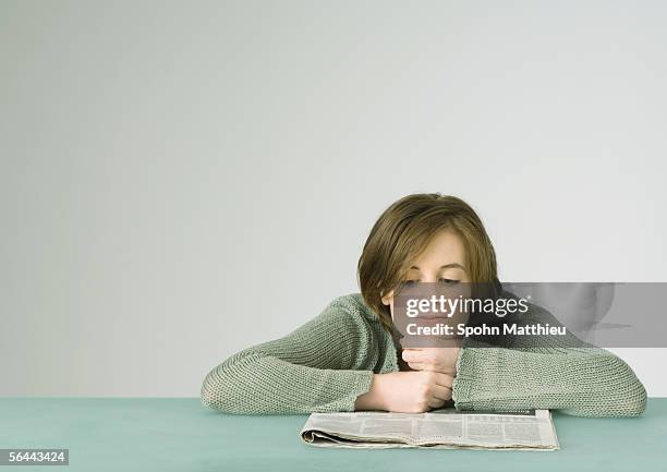 young woman leaning on table, reading newspaper - kin in de hand stockfoto's en -beelden