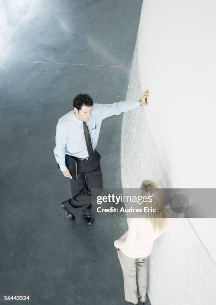 businessman and businesswoman leaning against wall and talking, high angle view - verführung büro stock-fotos und bilder
