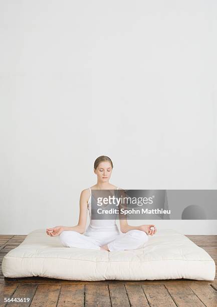 young woman sitting in lotus position on futon mattress - mattress stock pictures, royalty-free photos & images