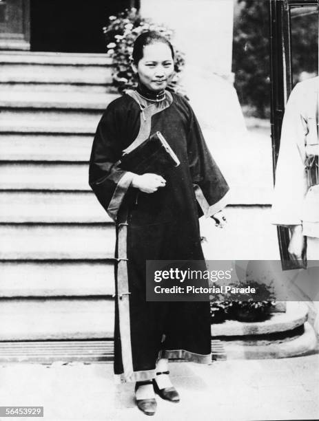 Chinese political figure Ching-ling Soong , better known as Madame Sun Yat-sen, holds a book under her arm as she stands on the curb while a soldier...