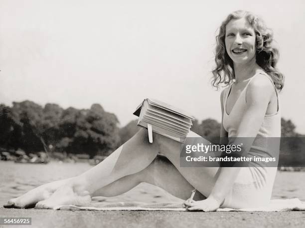 London: Sunbathing girl in her bathing suit in Hyde Park, smoking a cigarette and reading a book. Photography, 1932. [London: Maedchen in Badeanzug...