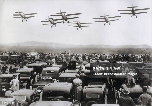 Formation flight of an aircraft squadron at the Great Flight Festival in Hendon near London. In the front numerous visitors?cars. Photography. 1933....