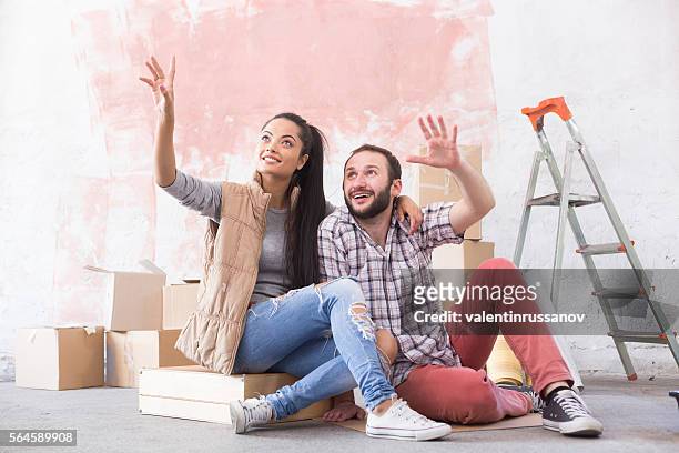 young couple making plans for home improvement - couple seated apartment hipster imagens e fotografias de stock