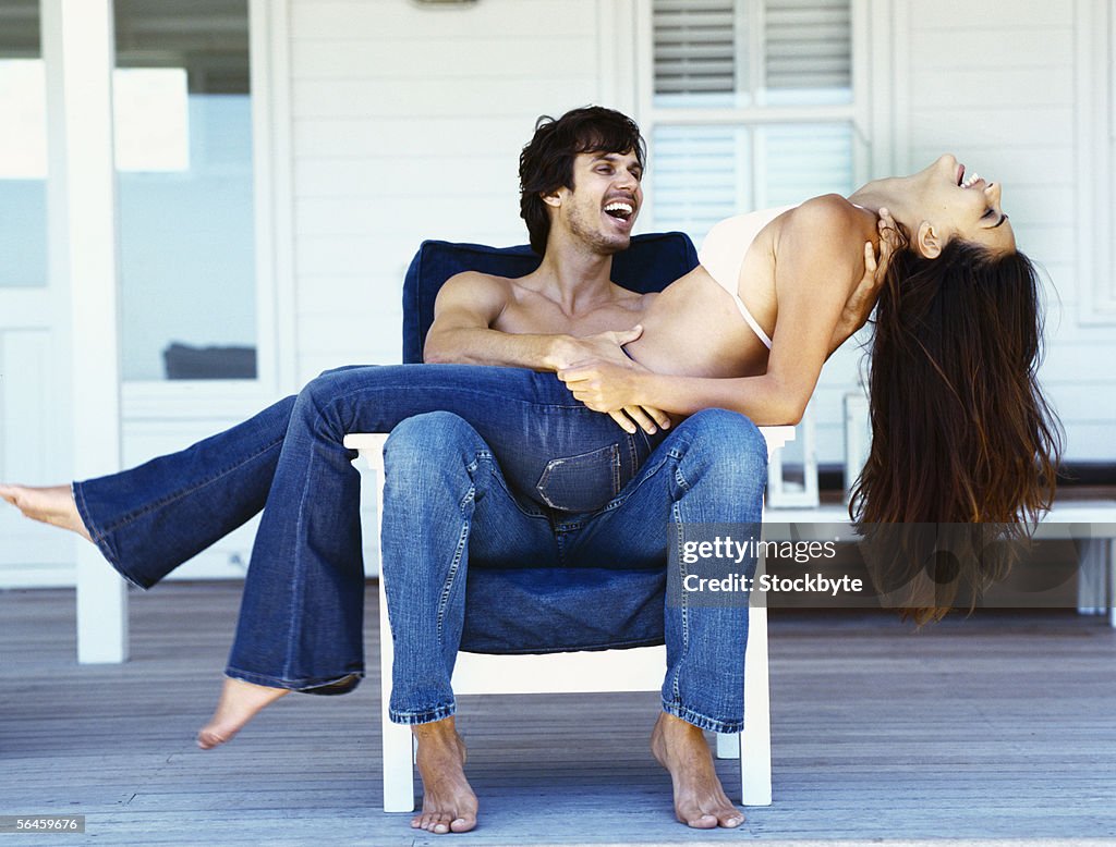 Young woman sitting on a young man's lap on an arm chair