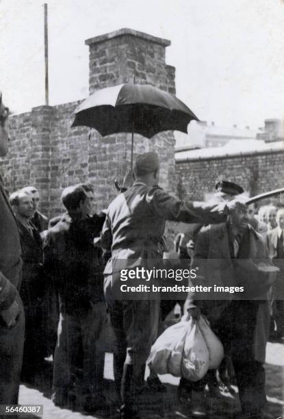 Holocaust: a Jewish man is holding a sunshade over a German soldier instructing Jews arriving in the concentration camp. Poland. Photography. About...