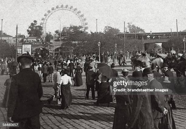 Viennese Prater. In the background the "Riesenrad" . Photography by M. Manenizza. Around 1900. [Auf dem Weg in den Wiener Wurstelprater, im...