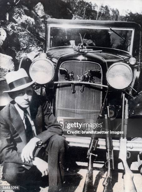 Gangster Clyde Barrow kneeing besides his automobile. Photography. [Der Verbrecher Clyde Barrow bewaffnet vor seinem Auto. Photographie.]