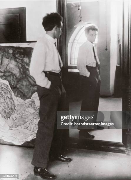 Egon Schiele , austrian painter standing in front of a mirrow in his studio. In the background the painting "The death an the maid" . Photography...