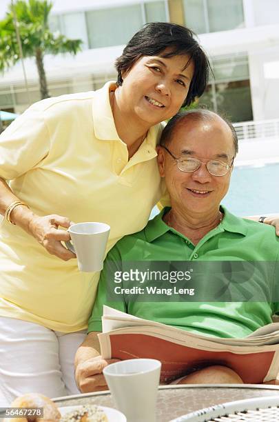 woman holding coffee mug, man sitting down holding newspaper, looking at camera - asian water polo cup foto e immagini stock