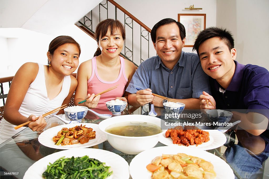 Family at home, sitting side by side, looking at camera, food on the table