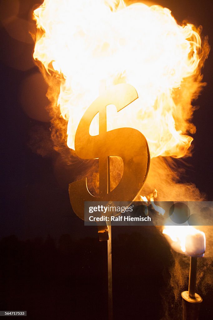 Metallic dollar sign set on fire at night