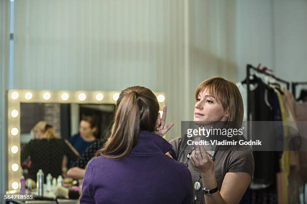 mature female artist applying make-up to model at studio - visagist stockfoto's en -beelden