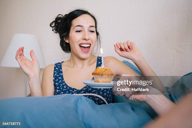surprised young woman blowing out candle on cupcake held by man at home - cupcake bildbanksfoton och bilder
