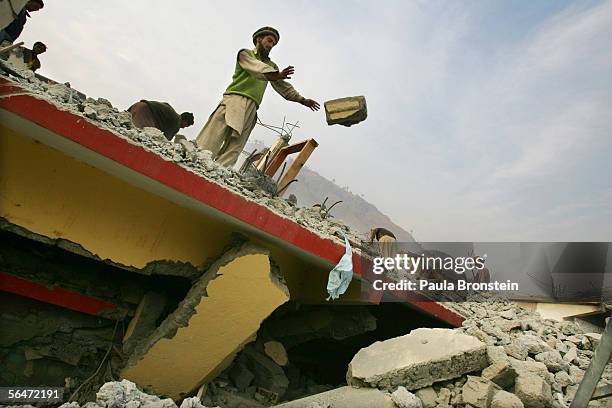 Pakistani men clear rubble from a shop December 20, 2005 in Muzaffarbad, Pakistan. Lack of snow is giving the quake survivors a break, but they are...