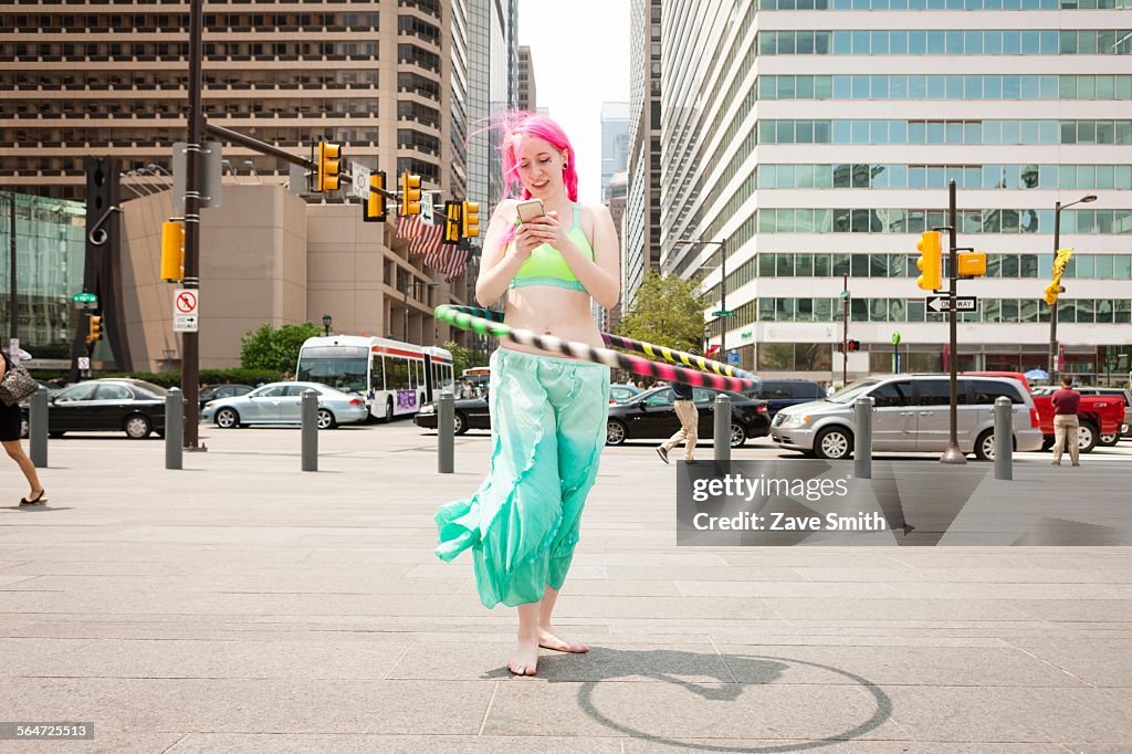 Young woman hoola hooping whilst reading smartphone text, Philadelphia, Pennsylvania, USA