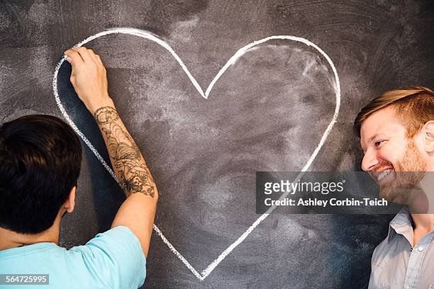 Male couple drawing heart on blackboard
