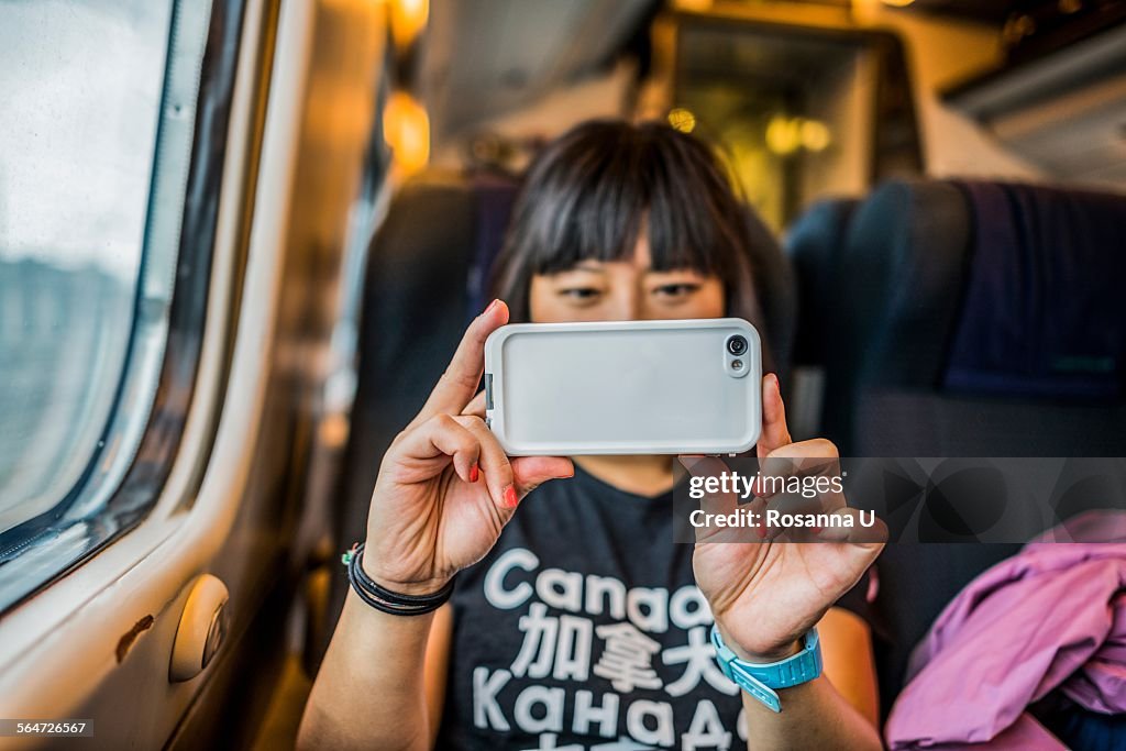 Woman on train using smartphone to take photograph