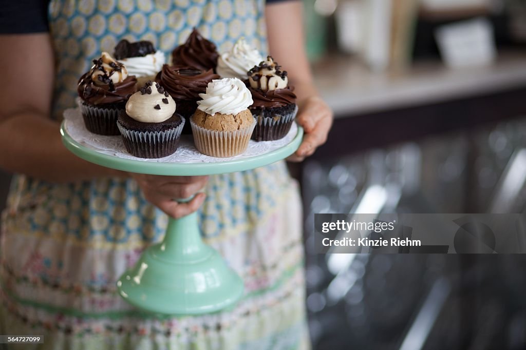 Bakery owner carrying tray of allergy-friendly cupcakes
