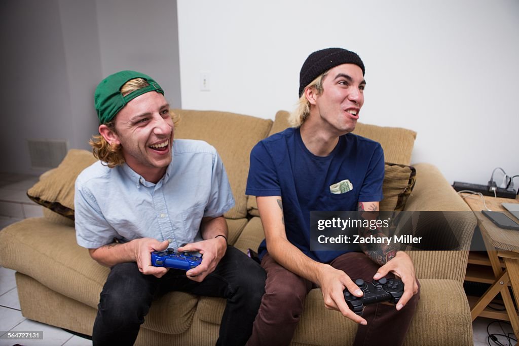 Two young men sitting on sofa, playing video game