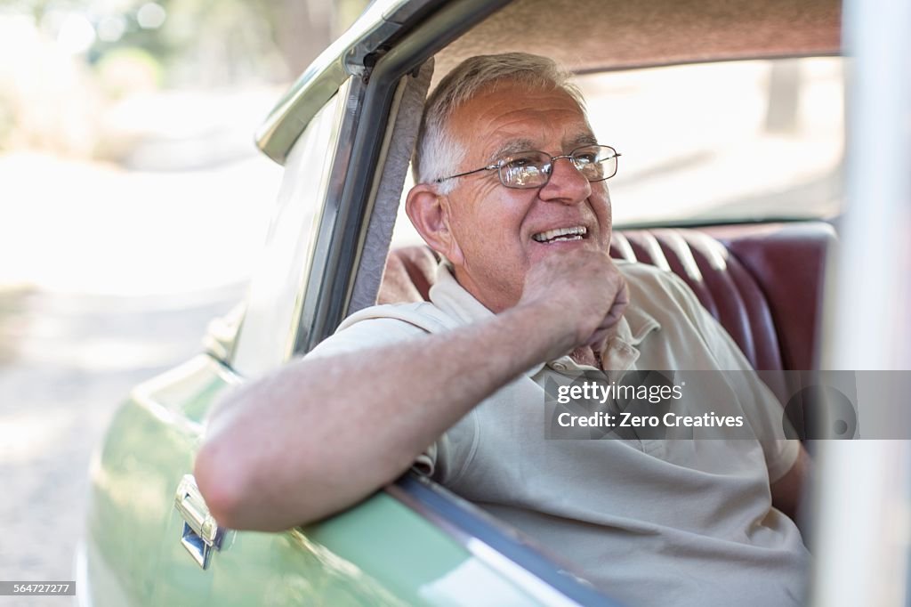 Senior man sitting in back seat of car, smiling